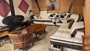 A cozy cabin interior with a sofa, a fireplace, a dining table, and a wooden ceiling. - Le Grand Chalet (Gérardmer)