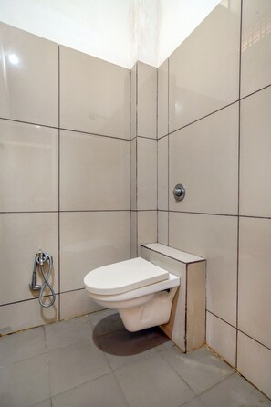 Un baño pequeño con azulejos, un inodoro blanco, un cabezal de ducha y una tubería visible.