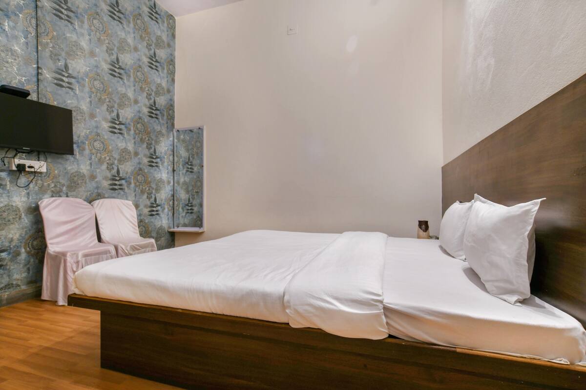 Une chambre avec un grand lit, un téléviseur fixé au mur et un papier peint à motifs sur le mur de gauche.