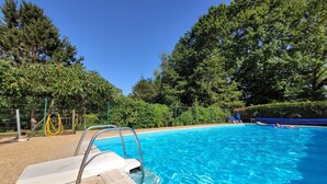 Una piscina con trampolín, rodeada de árboles y una cerca.