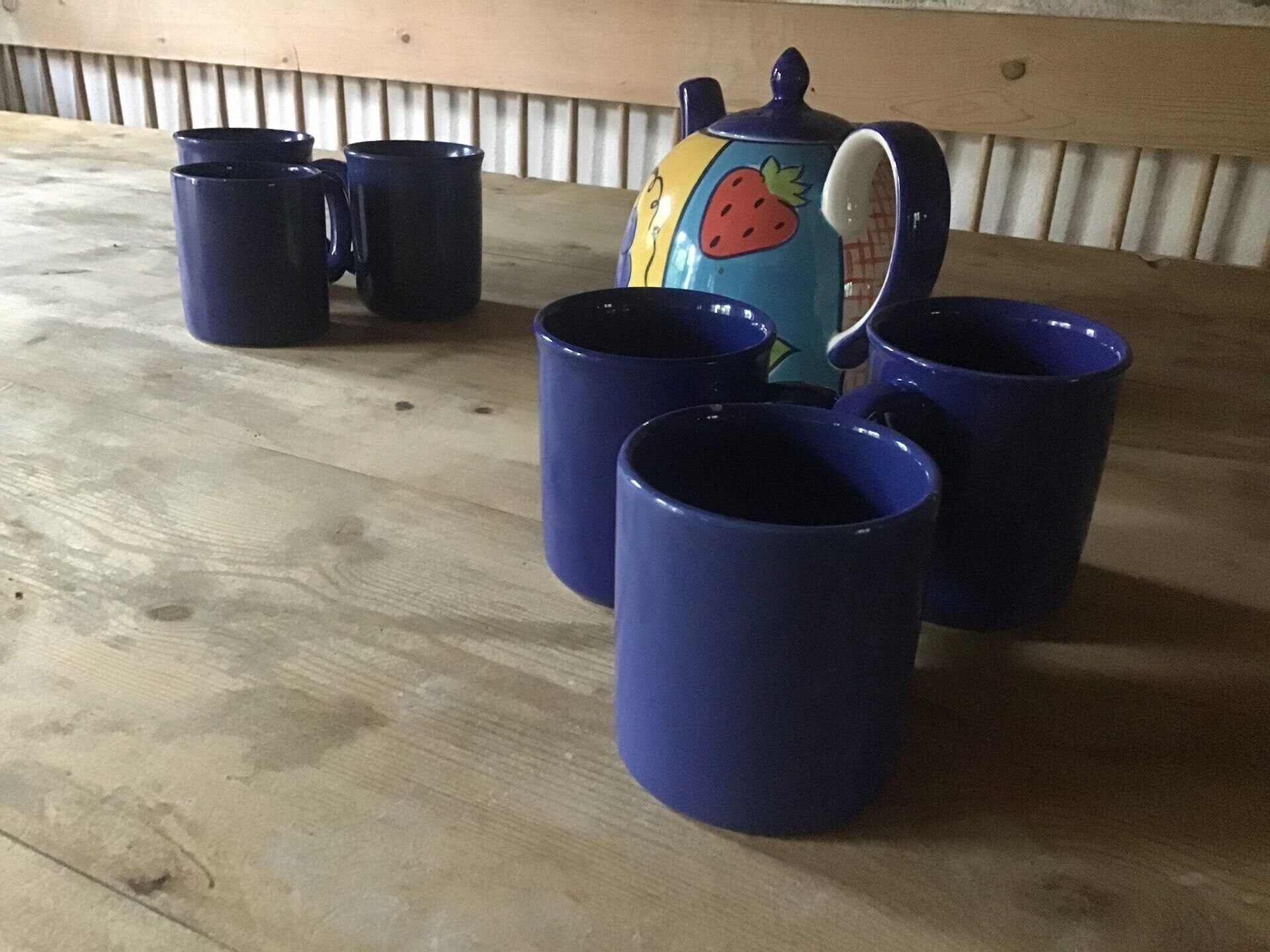 Ein Holztisch mit vier dunkelblauen Tassen und einer bunten Teekanne.