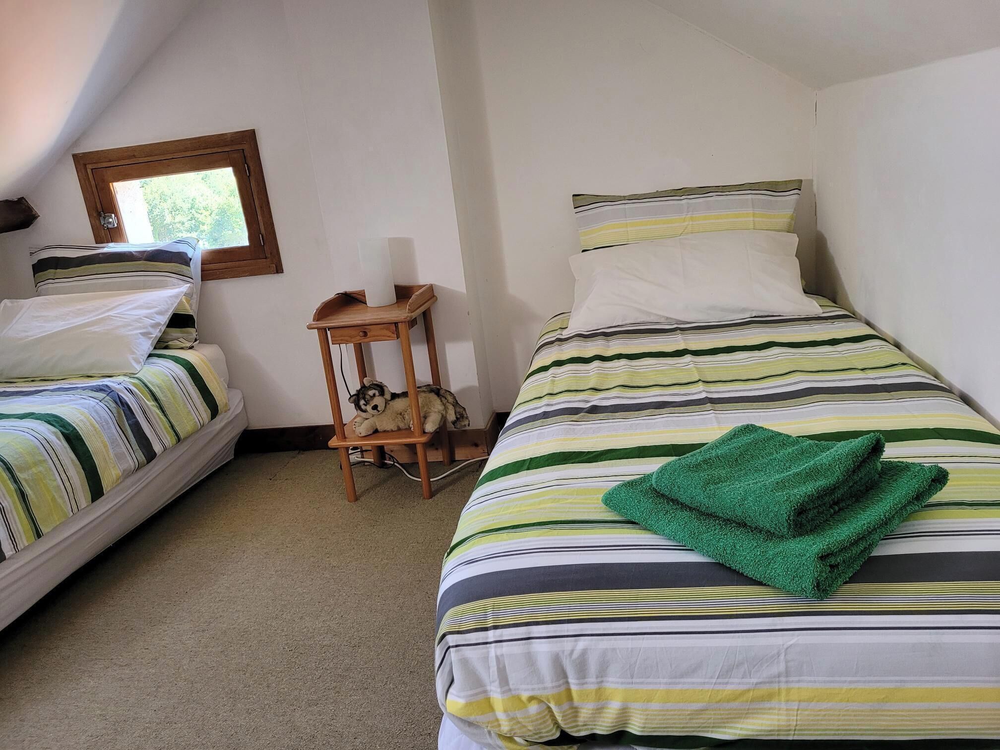Quarto com duas camas, uma mesa de cabeceira de madeira e uma janela.