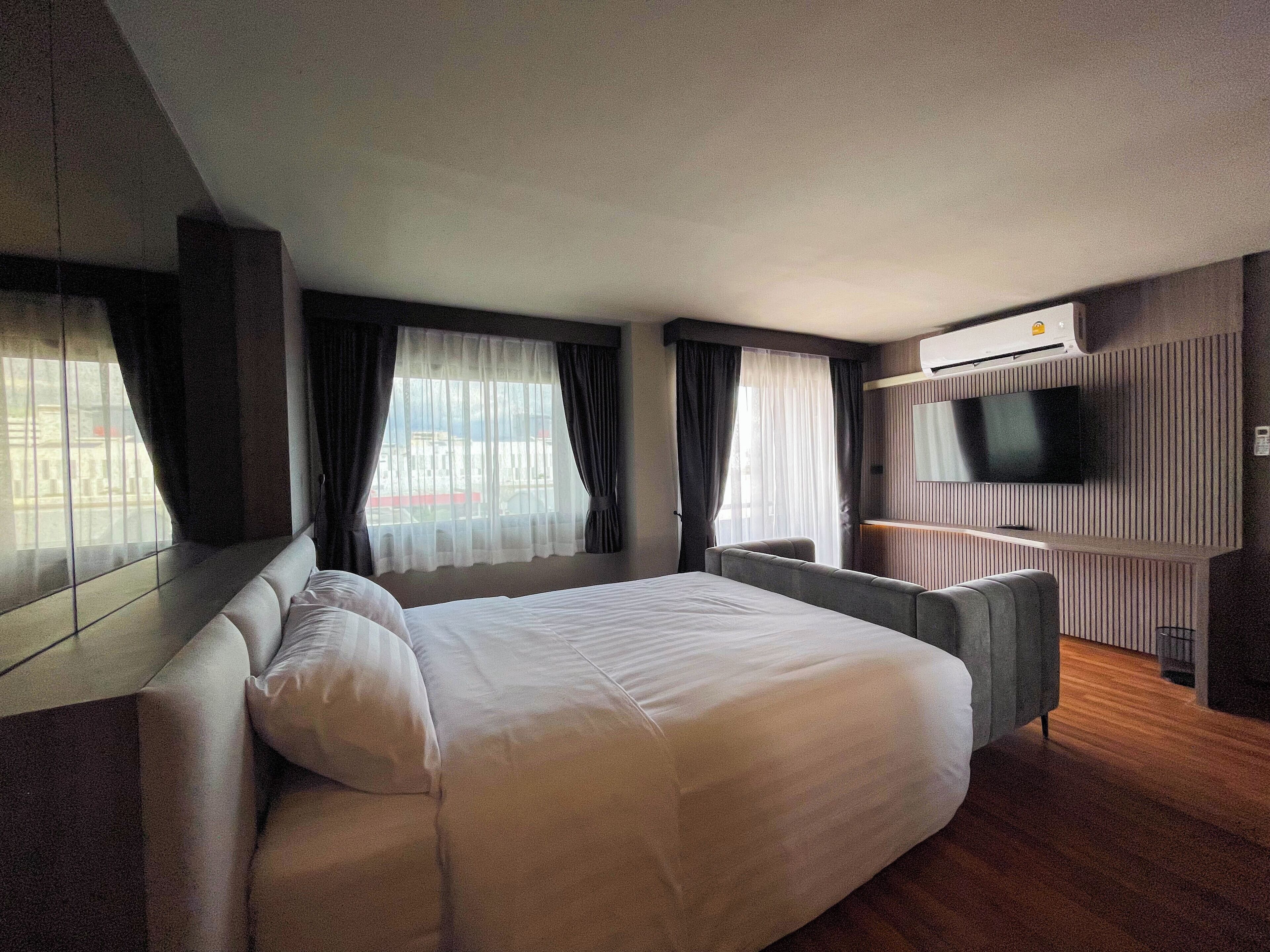 A modern hotel room with a large bed, a seating area, a flat-screen TV, and a view of the cityscape through the windows.