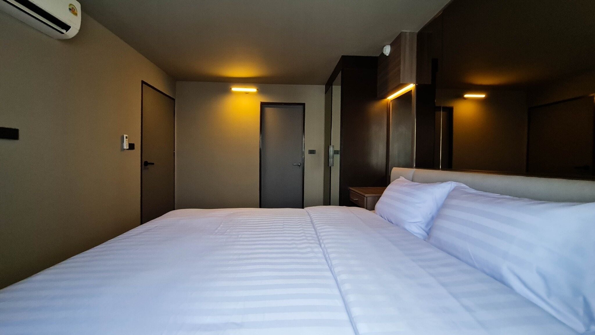 A hotel room with a large bed, a bedside table, a mirror, and an air conditioning unit.