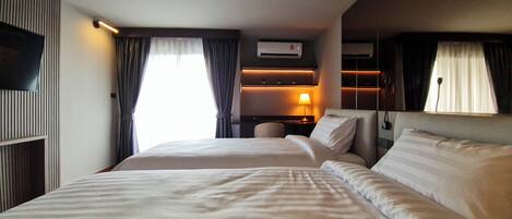 Habitación de hotel con dos camas, televisión, aire acondicionado, escritorio con lámpara y ventana con cortinas.