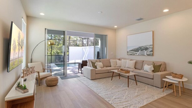 Una sala moderna con un sofá beige, una mesa de centro y un ventanal con vista a una piscina.