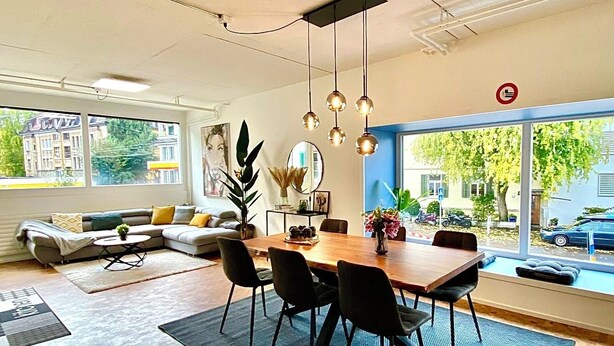 A modern living room with a dining area, large windows, and a view of the street. - 120m2 stylish 3-bedroom flat (Zürich)