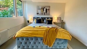 A bedroom with a large bed, a window, a radiator, a bedside table with a lamp, and a framed picture on the wall. - 120m2 stylish 3-bedroom flat (Zürich)