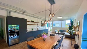 A modern kitchen with a built-in oven, a dining area with a wooden table and chairs, and a living area with a sofa and a coffee table. - 120m2 stylish 3-bedroom flat (Zürich)