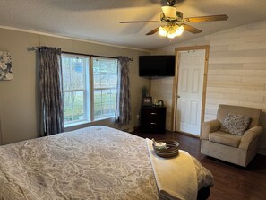A bedroom with a bed, a chair, a television, and a door.