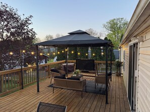 Une terrasse extérieure couverte, aménagée avec des meubles en osier, un téléviseur et des guirlandes lumineuses.