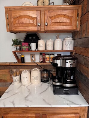 A kitchen with wooden cabinets, a coffee maker, and labeled containers for sugar, tea, and coffee.