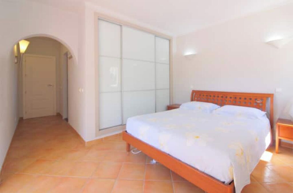 A bedroom with a bed, a nightstand, a sliding glass door, and a tiled floor.