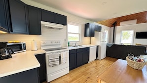A modern kitchen with black cabinets, a white stove, and a wooden dining table. - Brackley Rose- Charming Water Front Cottage In Brackley, Minutes To Beaches (Brackley Beach)