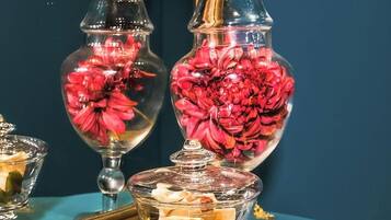 A mirror reflecting three glass vases with flowers, a small glass bowl, and a gold-framed mirror on a teal surface.