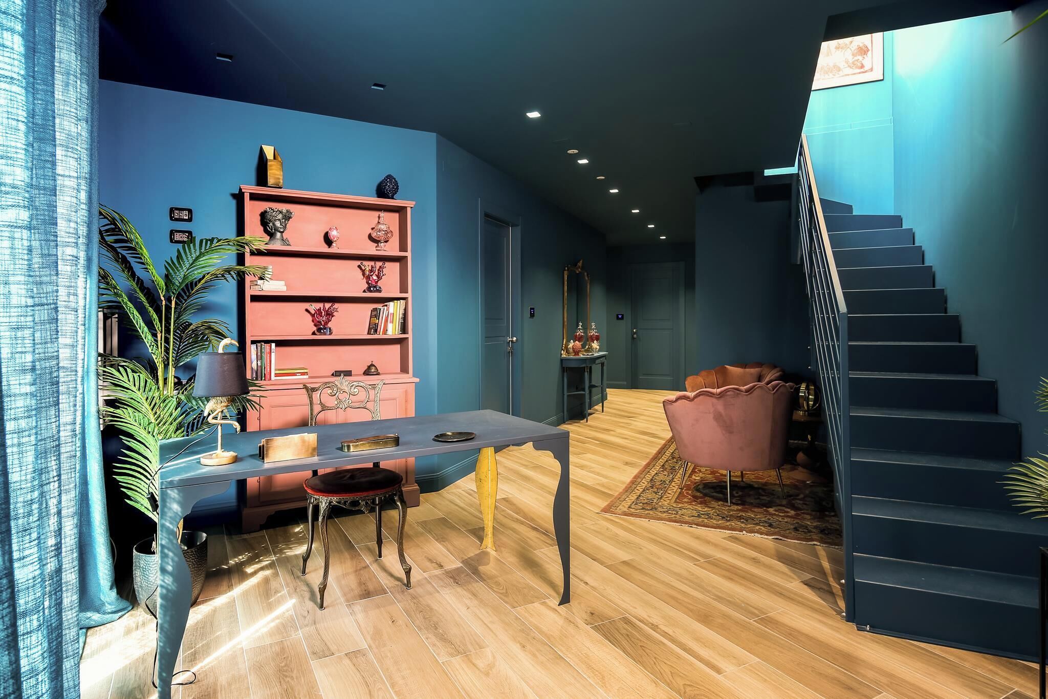 Un intérieur moderne comprenant un escalier, un coin repas avec une table et des chaises, et une bibliothèque agrémentée d’objets décoratifs.
