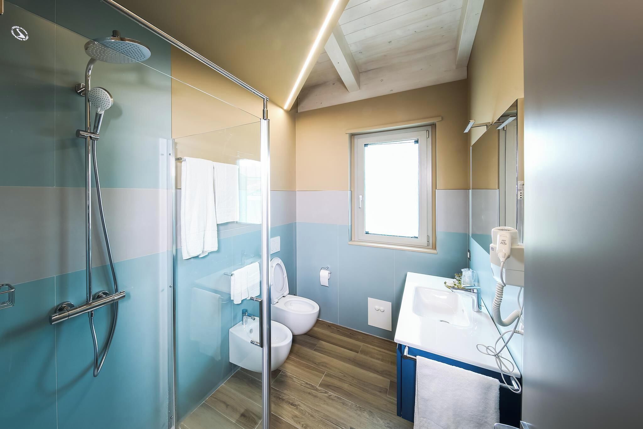 A bathroom with a glass-enclosed shower, a toilet, and a sink with a hairdryer.