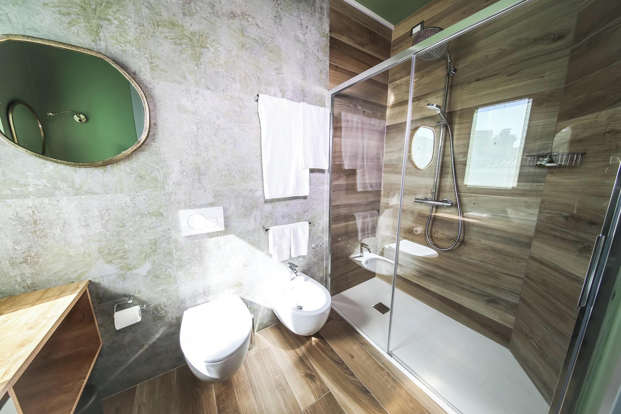 Un baño moderno con ducha envuelta en vidrio, tocador de madera, inodoro y un espejo grande.