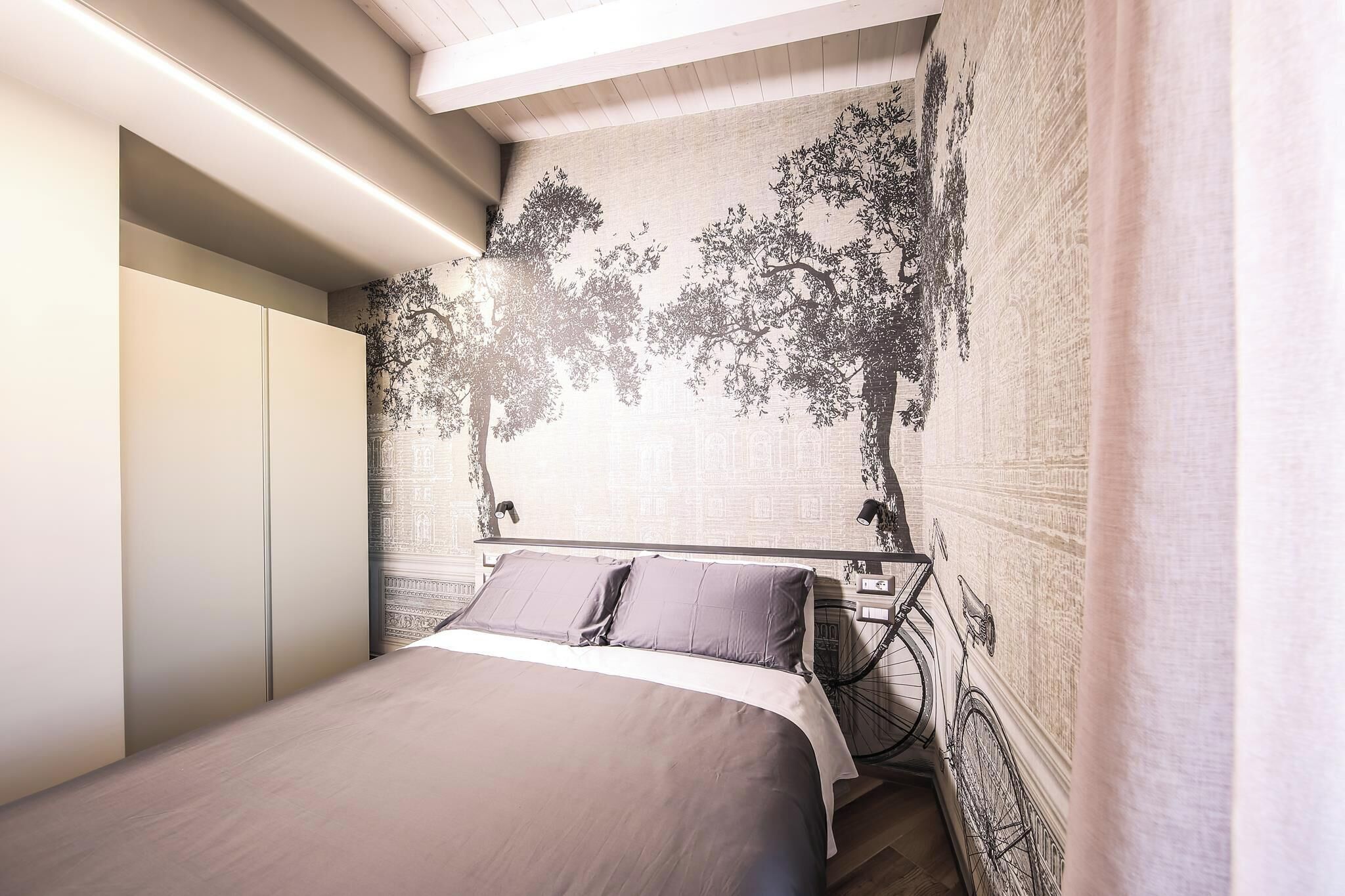 A bedroom with a bed, a bicycle, and a wall with a tree mural.