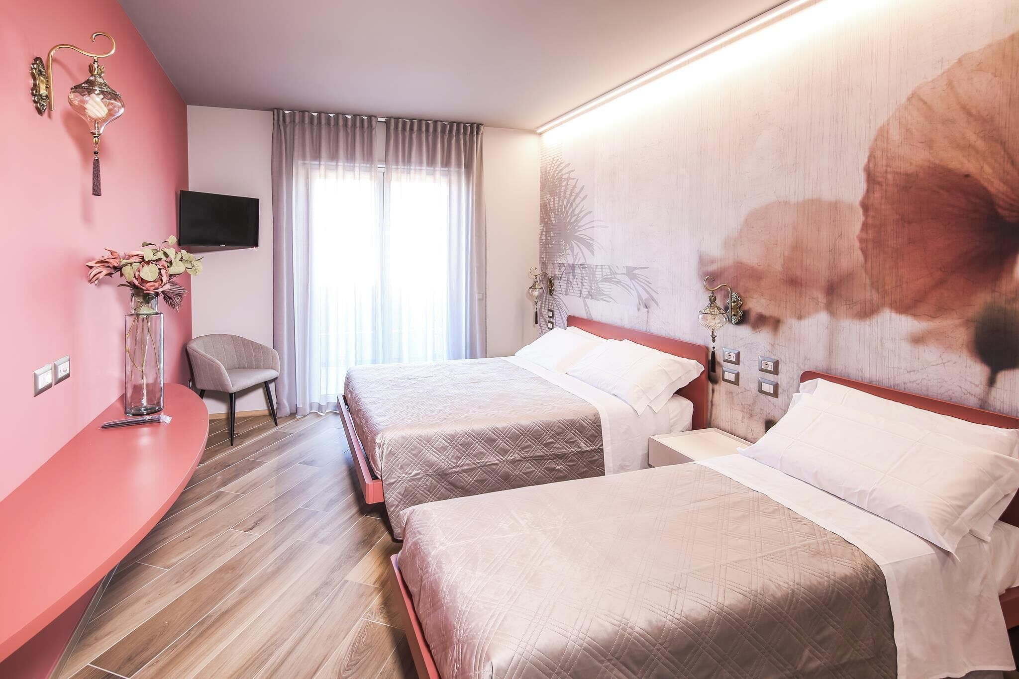 A hotel room with two beds, a TV mounted on the wall, a chair, and a large floral artwork on the wall.