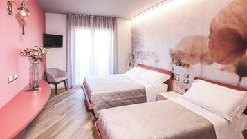 A hotel room with two beds, a TV mounted on the wall, a chair, and a large floral artwork on the wall.
