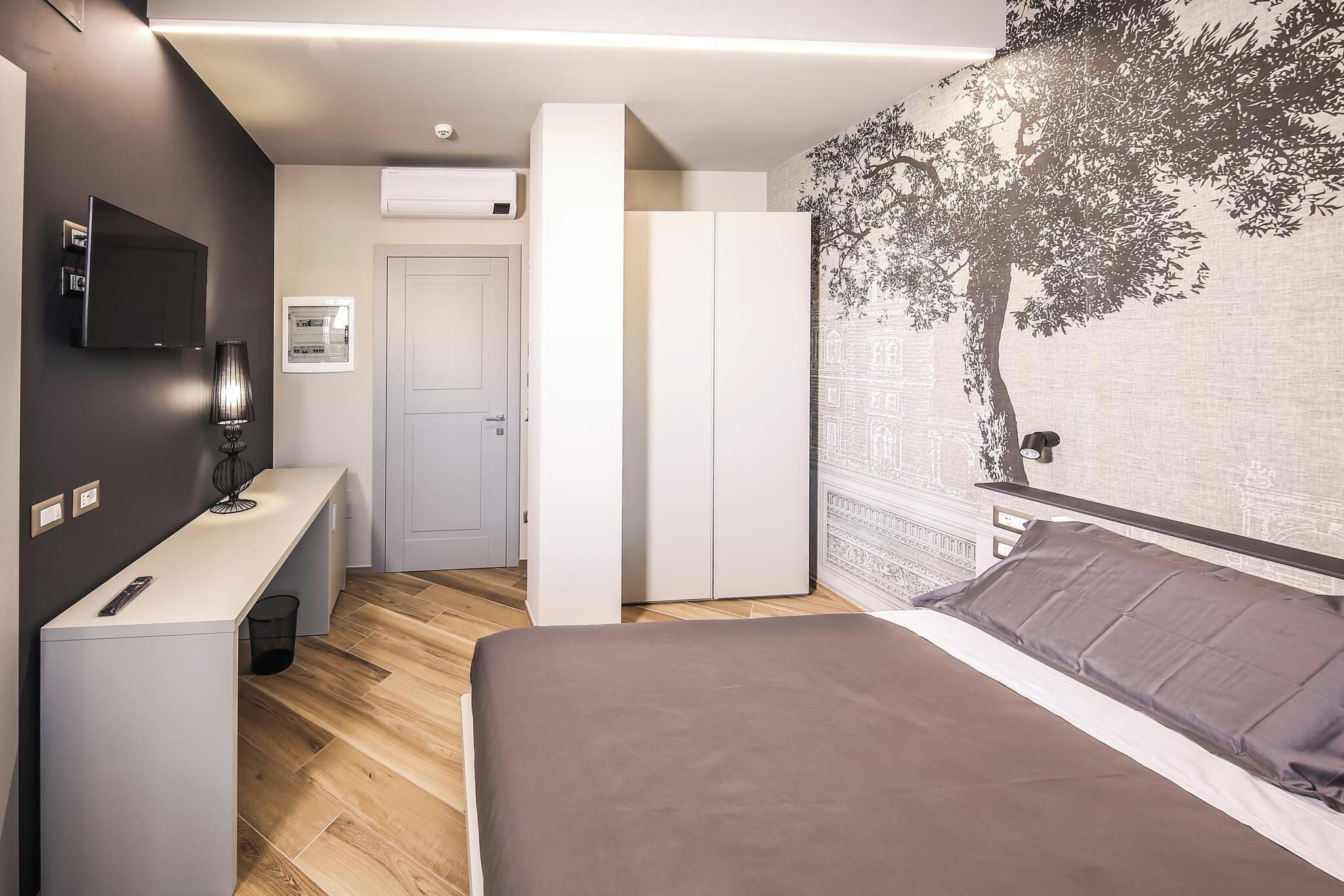 A modern bedroom with a bed, a desk, a TV, and a wardrobe.