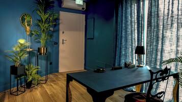 Une pièce avec un plancher en bois foncé, une table noire avec une chaise, et plusieurs plantes en pot.