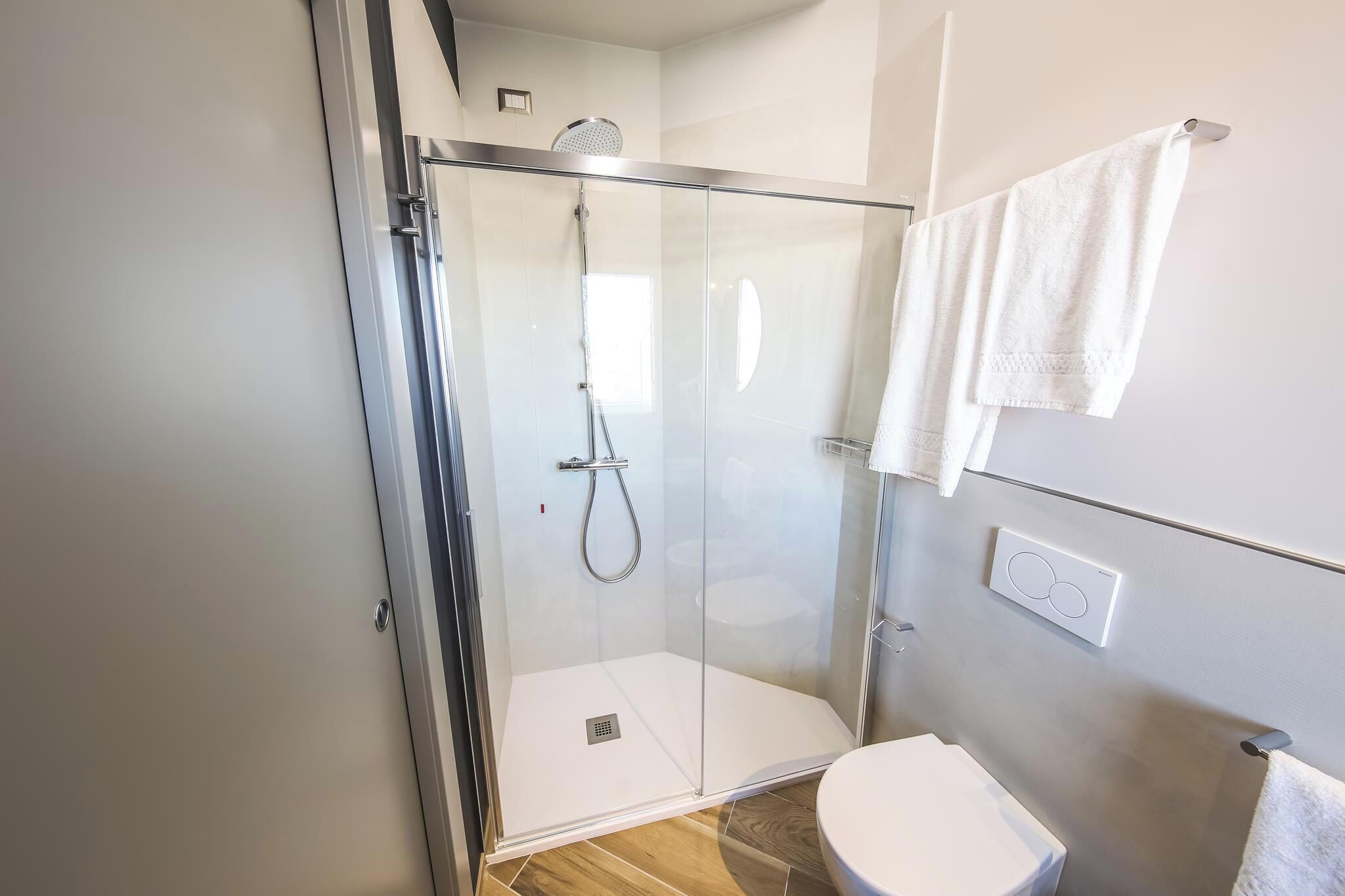 A modern bathroom with a glass-enclosed shower, a toilet, and a towel rack.