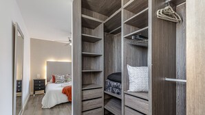 En walk-in-garderob med hyllor i trä, en säng med mönstrat sänglinne och en spegel.