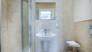 A bathroom with a glass shower enclosure, a pedestal sink, a mirror above the sink, and a towel rack. - Spacious 2 bed in Pimlico (London)