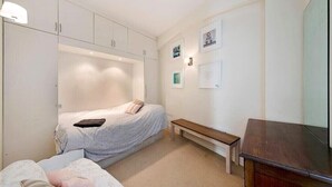A bedroom with a bed, a bench, a dresser, and wall-mounted pictures. - Spacious 2 bed in Pimlico (London)