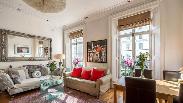 A living room with a sofa, coffee table, and dining table. There are windows with curtains, a painting on the wall, and a mirror above the sofa. - Spacious 2 bed in Pimlico (London)
