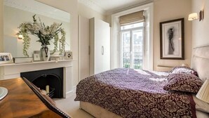 A bedroom with a large bed, a fireplace, a mirror, and a window with a view. - Spacious 2 bed in Pimlico (London)