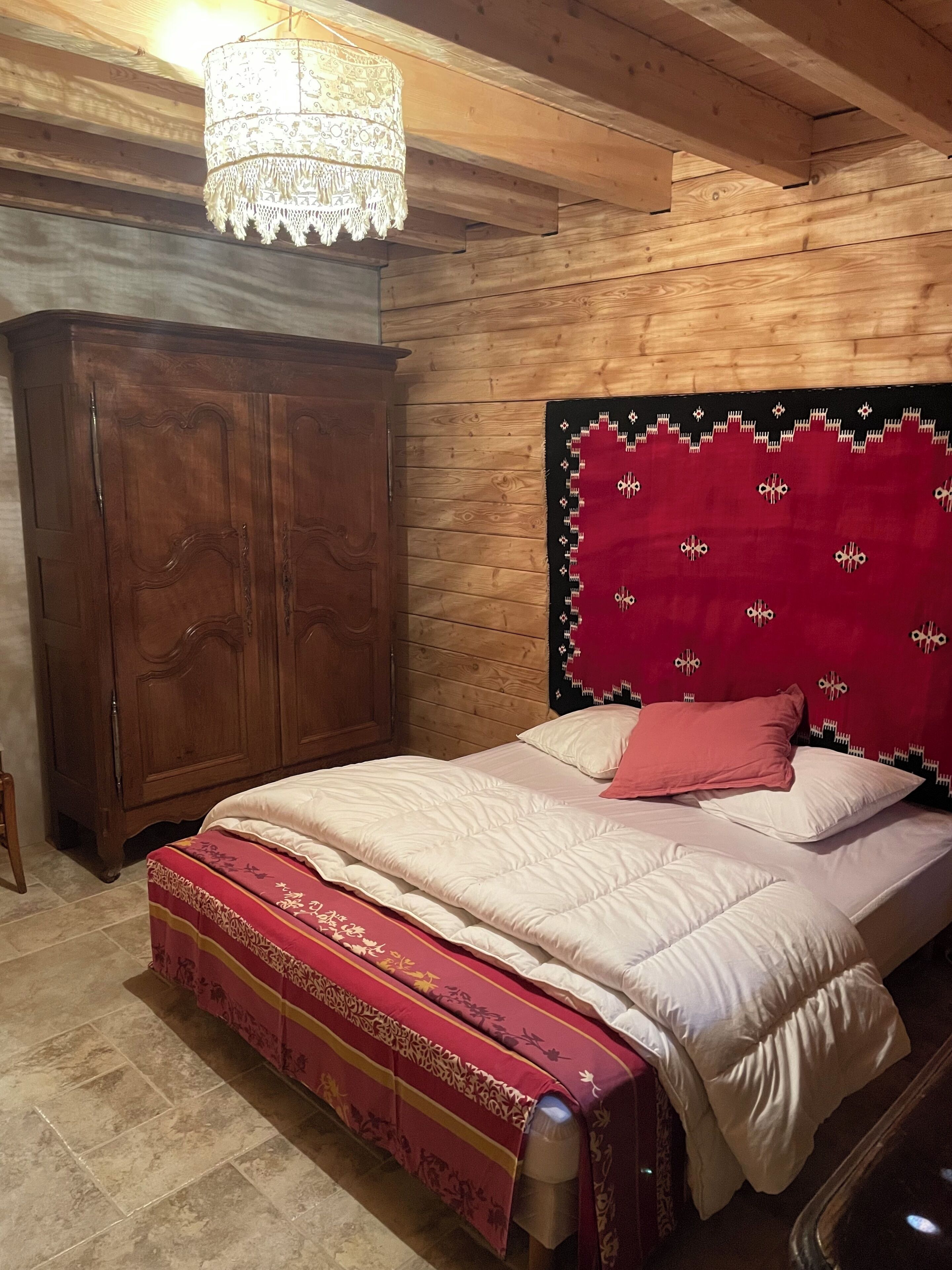 Quarto com painéis de madeira, uma cama, um guarda-roupa e um candeeiro suspenso.