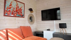 Habitació amb interior de fusta, un gran televisor de pantalla plana penjat a la paret, un mirall rodó i un sofà amb coixins taronja.