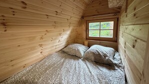 A small, wooden cabin room with a single bed, a window, and a sloped ceiling. - Logement Insolite Cabane Pod sur Pilotis (Valencisse)
