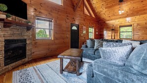 A cozy cabin interior with a stone fireplace, wooden walls, a sofa, and a small table.