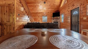 A wooden interior with a dining table, two circular placemats, a sofa, and a staircase.