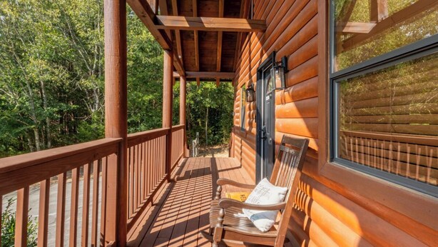 A wooden deck with a bench and a window overlooking a forest.