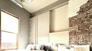 Ein Zimmer mit zwei Betten, einer Steinwand, einem großen Fenster und einem Deckenventilator.