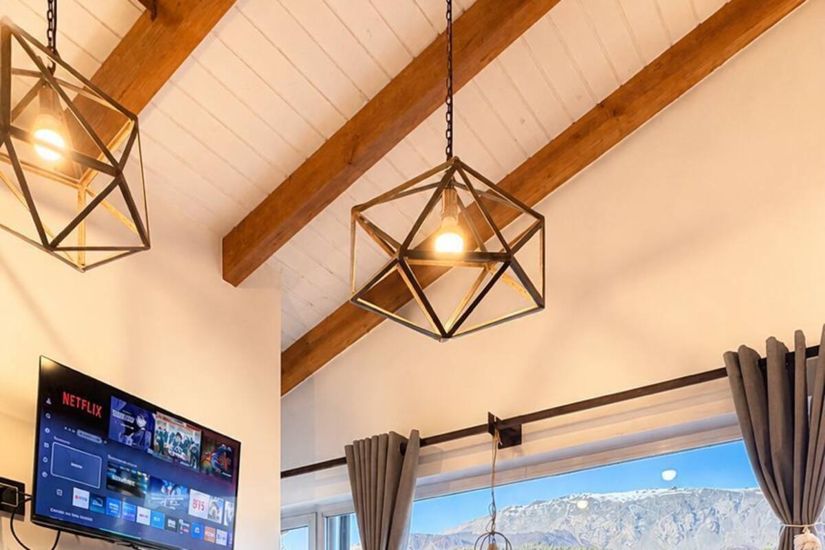 Une chambre à coucher avec un lit, un téléviseur fixé au mur, une fenêtre avec des rideaux et une vue sur un paysage montagneux.
