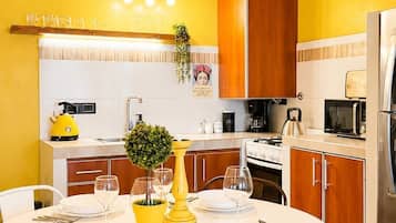 A modern kitchen with a round dining table, white and wooden cabinets, a hanging light fixture, and a yellow wall.