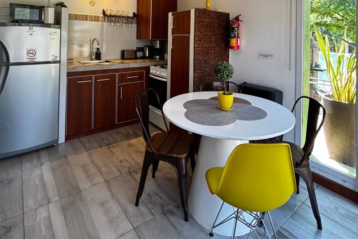 Una cocina moderna con armarios de madera, un refrigerador de acero inoxidable y un comedor con una mesa redonda y sillas amarillas.