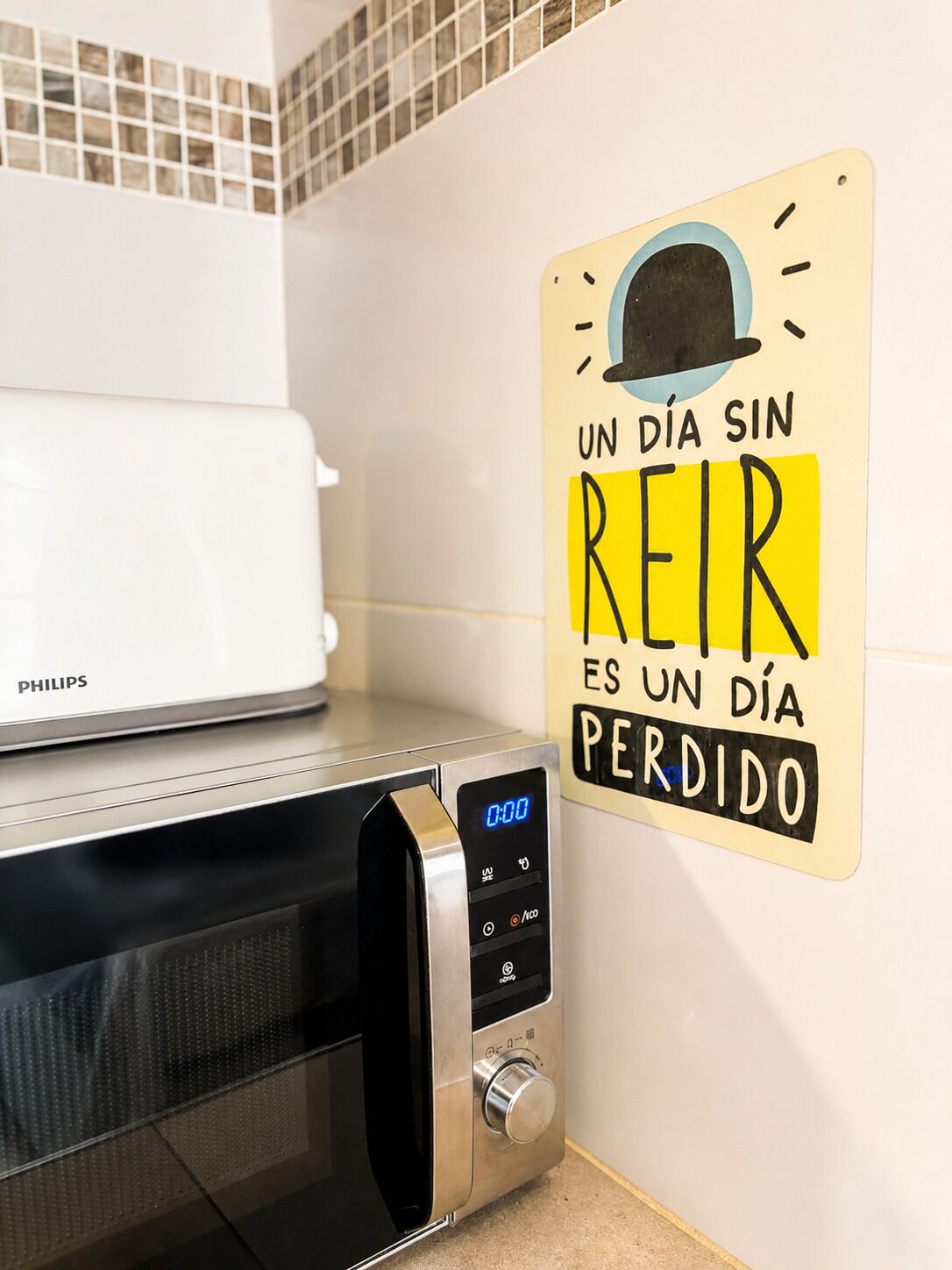 A kitchen with a microwave, a toaster, and a sign on the wall.