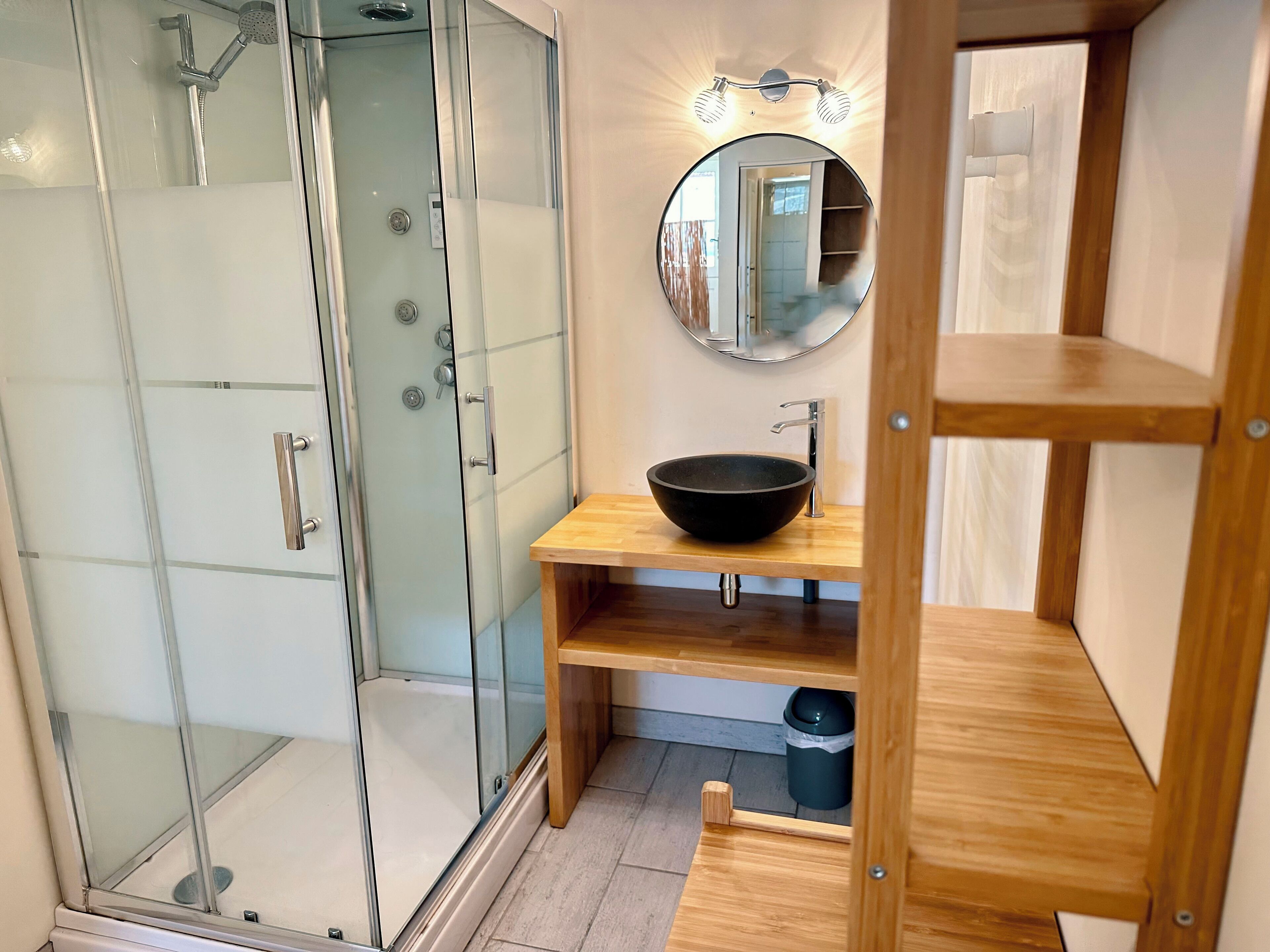 Une salle de bain moderne avec une douche à parois de verre, un meuble-lavabo en bois avec un vasque noire et un miroir au-dessus du lavabo.