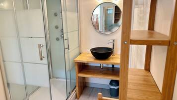 Une salle de bain moderne avec une douche à parois de verre, un meuble-lavabo en bois avec un vasque noire et un miroir au-dessus du lavabo.