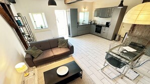 A modern living room with a sofa, coffee table, and a dining area with a glass table. - Gite Alcea - Château de Panisseau (Thénac)