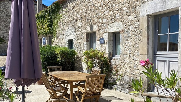 An outdoor seating area with a stone building, wooden furniture, and a potted plant. - Gite Alcea - Château de Panisseau (Thénac)