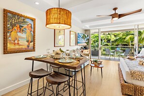 A dining area with a wooden table set for four, bar stools, and a large woven pendant light. - Ocean View steps from beach, dining, shopping 418 (Lahaina)