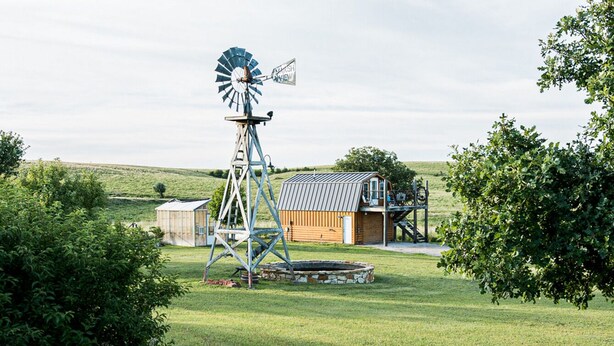 A windmill, a wooden barn, and a small house in a grassy field.